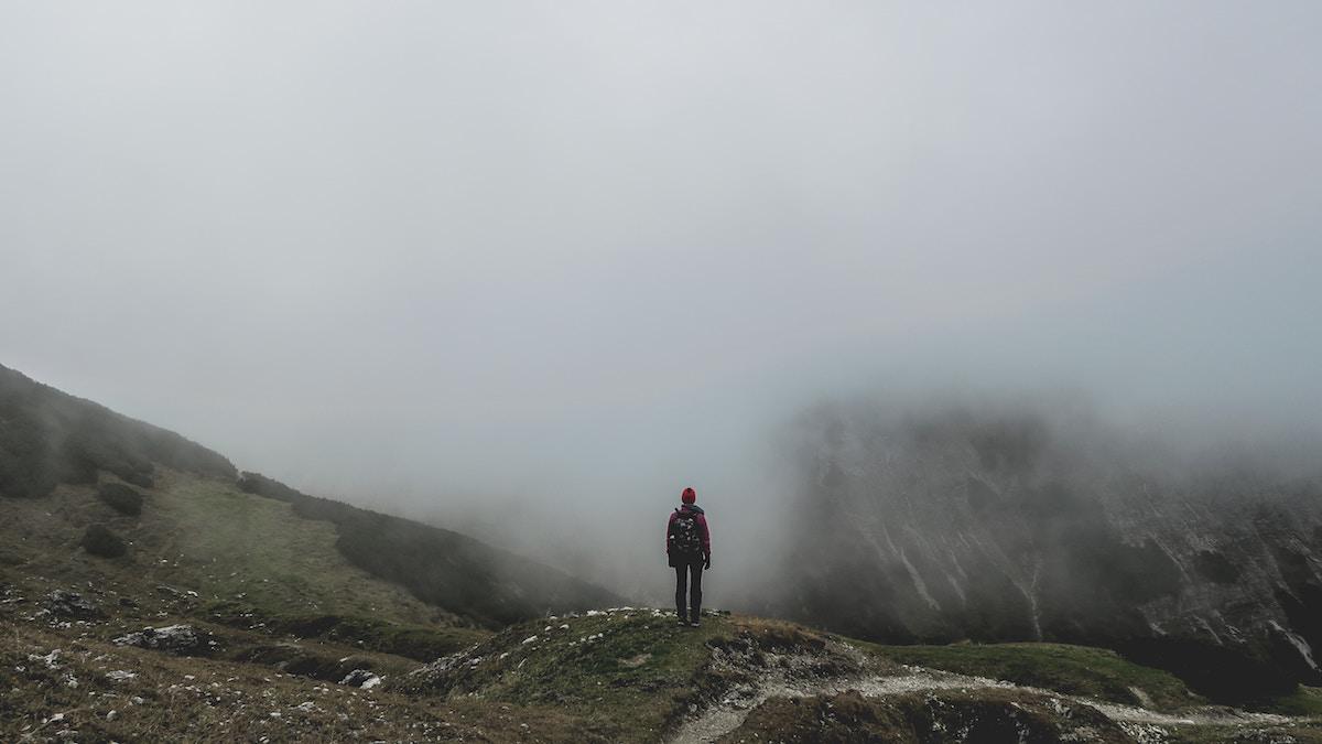 Lonely person standing on a mountain surrounded by fog